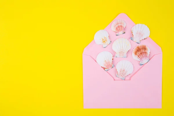Rosa Umschlag mit vielen Jakobsmuscheln auf gelbem Backgro — Stockfoto