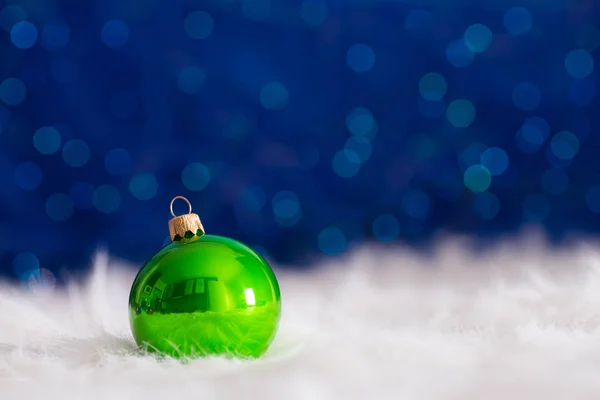 Zielony Boże Narodzenie ball na białe futro z świateł girlanda na niebieski bo — Zdjęcie stockowe
