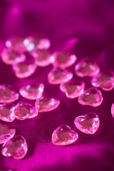 Muchos pequeños corazones de cristal rosa en tela de satén carmesí —  Fotos de Stock