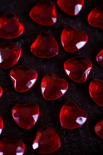 Många röda lilla kristall hjärtan på svart trä bakgrund. — Stockfoto