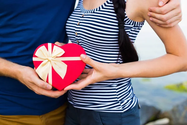Pareja romántica sosteniendo caja de regalo roja en forma de corazón — Foto de Stock