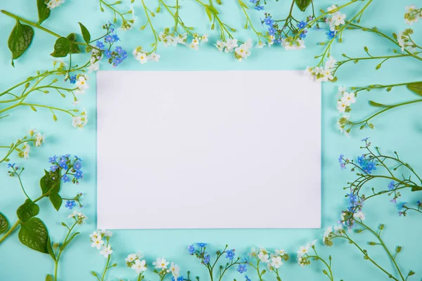 Clear sheet of white paper surrounded with blue and white little flowers on light mint background.