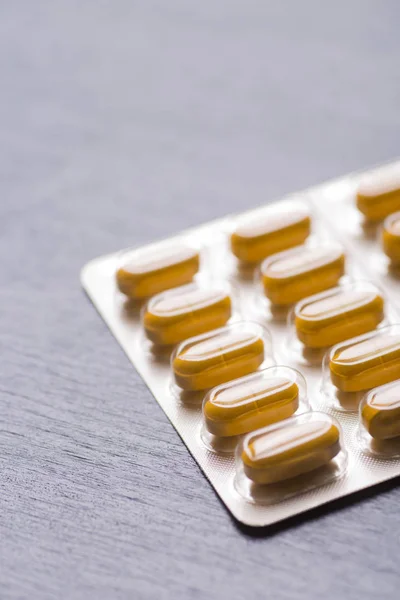Žluté dlouhé pilulky v blistru close-up na šedém pozadí — Stock fotografie