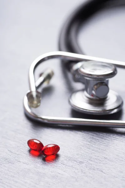 Closeup stethoscope near two red transparent capsules on gray table — Stock Photo, Image