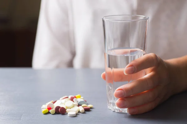 Hand holding glass of water near colorful different capsules and pills on table — Stock Photo, Image