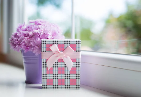 Petit seau violet avec bouquet tendre de belle oeillet rose avec boîte cadeau près de la fenêtre à la lumière du jour — Photo