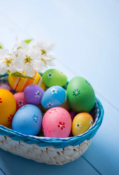 Vielfalt an verzierten bunten Ostereiern im Korb mit weißen Frühlingsblumen auf hellblauem Hintergrund — Stockfoto