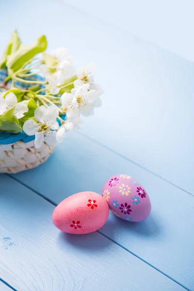 Dos huevos de Pascua pintados cerca de la cesta con rama floreciente de primavera blanca sobre fondo azul claro — Foto de Stock