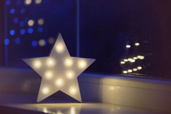 Белая звезда у окна на фоне гирлянд в вечернее время Лицензионные Стоковые Фото