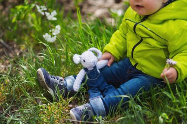 Küçük bebek çocuk örgü oyuncak beyaz tavşan tutarak ve çim açık bahar üzerinde oturan kot pantolon ve ceket