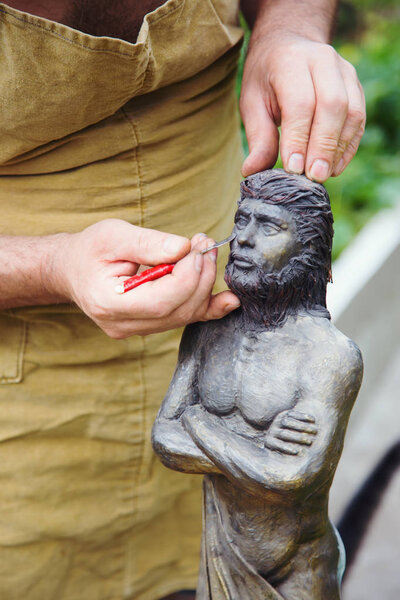 Closeup hands of sculptor in apron making sculpture of man using instrument outdoor
