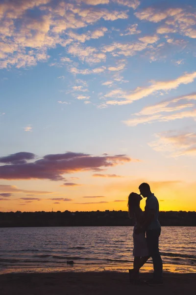 Silueta de pareja romántica en abrazo contra el cielo nublado en la puesta de sol cerca del lago — Foto de Stock