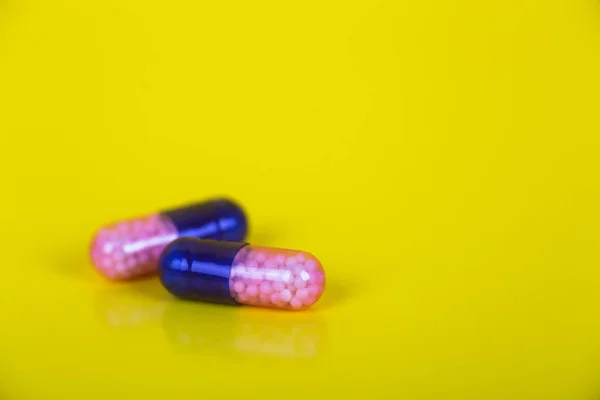 Closeup dva tmavě modré a růžové transparentní kapsle s mikro granule uvnitř na žlutém podkladu — Stock fotografie