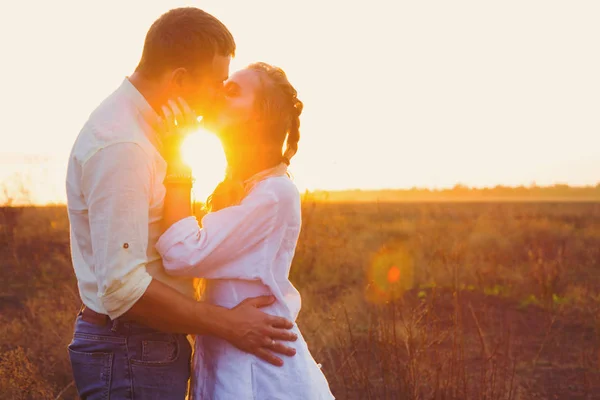 Joven hermosa pareja besándose contra la puesta de sol rayos al aire libre en el campo en la puesta de sol — Foto de Stock