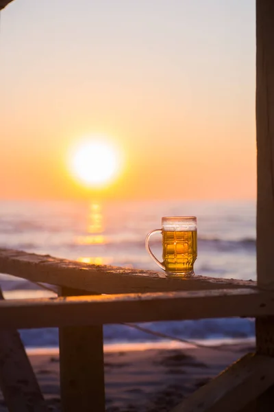 Полный стакан светлого пива на фоне рассвета на пляже Лицензионные Стоковые Изображения