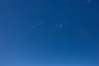 Uzakta bulutsuz gökyüzünde kavisli bir iz bırakan uçak. 2020 'nin Rengi - Klasik Mavi.