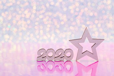 Wooden icon with 2020 digits and white New Year star on white glitter sparkling and pink background with bokeh