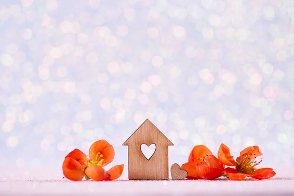 Closeup wooden house with hole in form of heart surrounded by spring flowering tree branches on glitter sparkling white background with bokeh.