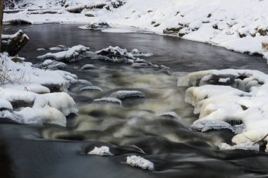 Kış ormanında buzla kaplı küçük bir nehir