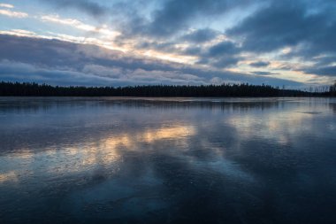 Mavi ve turuncu gün batımında bulutlar ve orman suya yansıyor. Finlandiya 'da gölün kenarında sessiz bir akşam. 