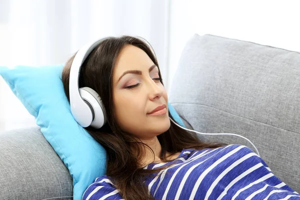 Jonge vrouw liggend op de Bank en het luisteren van muziek met koptelefoon — Stockfoto