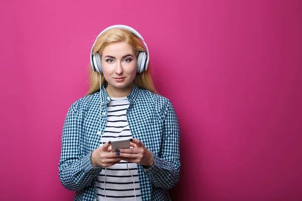 Jonge vrouw luisteren muziek met koptelefoon op roze achtergrond — Stockfoto