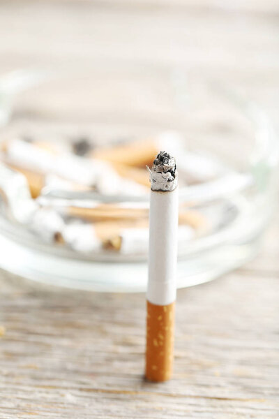 Сигарета с золой на сером деревянном столе
