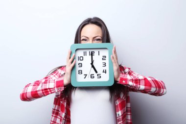 Gri arka plan üzerinde bir saat tutan genç kadın