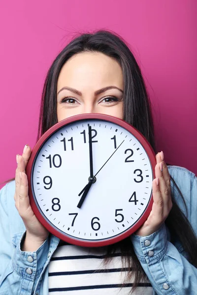 Mujer joven sosteniendo un reloj sobre fondo rosa — Foto de Stock