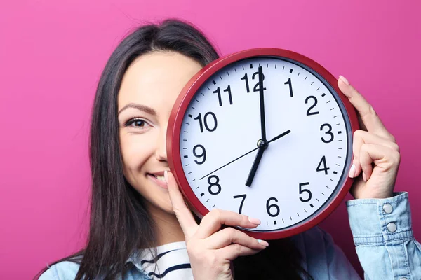 Bir saat, pembe arka plan tutan genç kadın