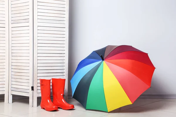 Stivali rossi con ombrello vicino schermo pieghevole in legno — Foto Stock