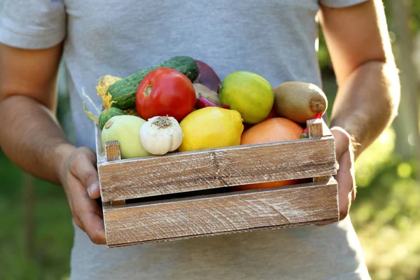 Seorang pria memegang peti dengan buah-buahan dan sayuran — Stok Foto