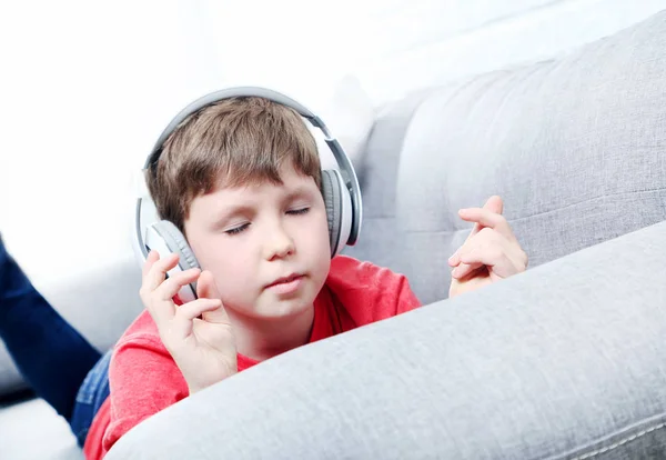 Portræt af ung dreng med hovedtelefoner på grå sofa - Stock-foto