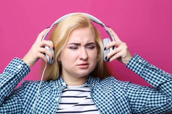 Jonge vrouw luisteren muziek met koptelefoon op roze achtergrond — Stockfoto