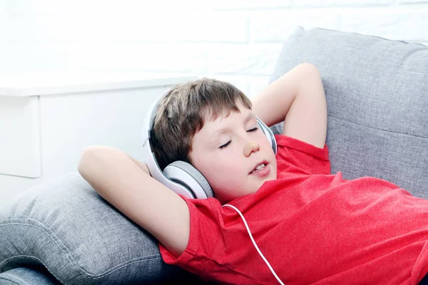 Portræt af ung dreng med hovedtelefoner på grå sofa - Stock-foto