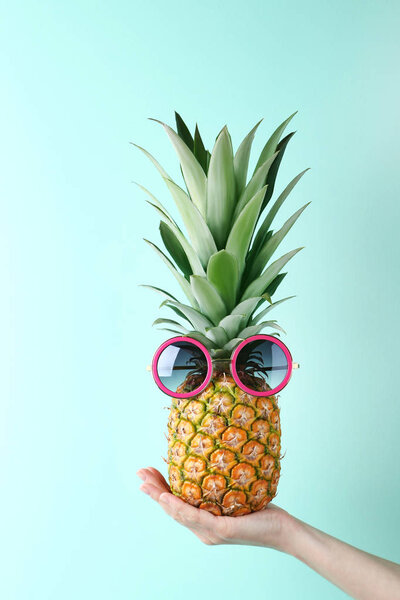 Female hand holding pineapple with sunglasses