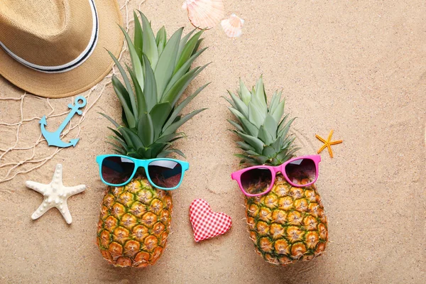 Pineapples with sunglasses and hat on sandy beach — Stock Photo, Image