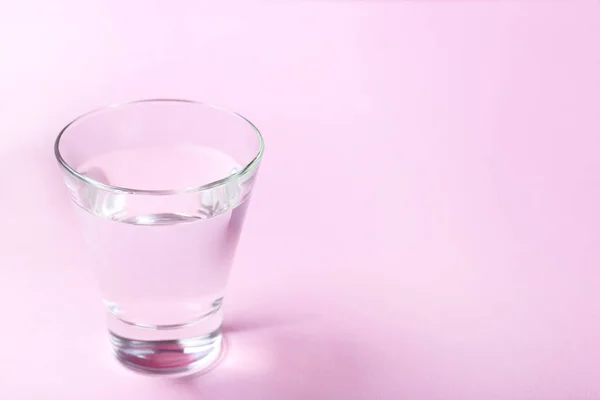 Vidro com água sobre fundo rosa — Fotografia de Stock