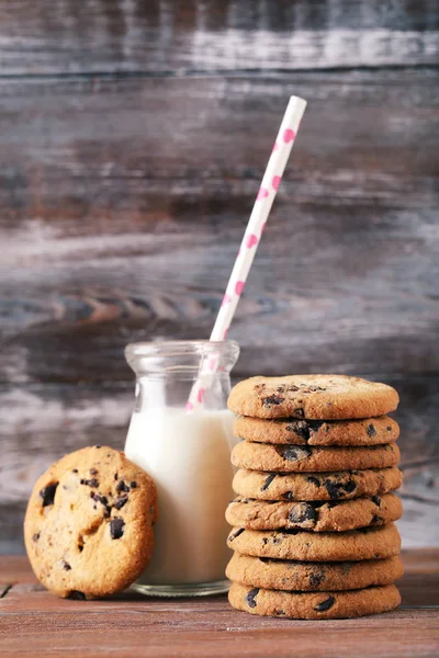 Chocolate chip cookies med flaska mjölk på brunt träbord — Stockfoto