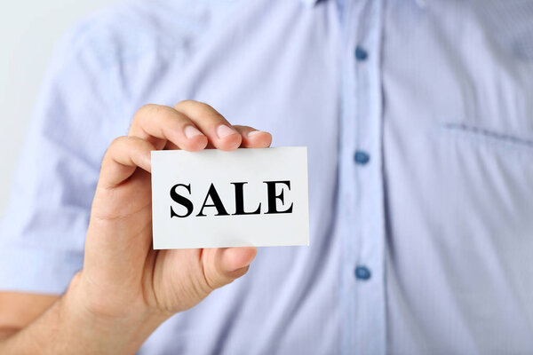 Мужчина держит визитку со словом Продажа
