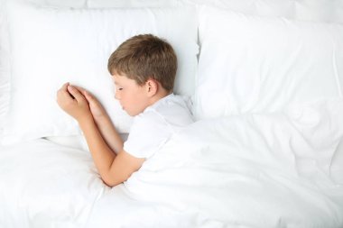 Beyaz yatakta uyuyan genç çocuk
