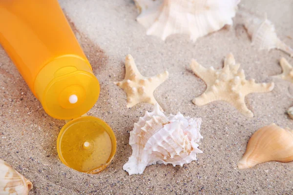 Protetor solar com conchas na areia — Fotografia de Stock