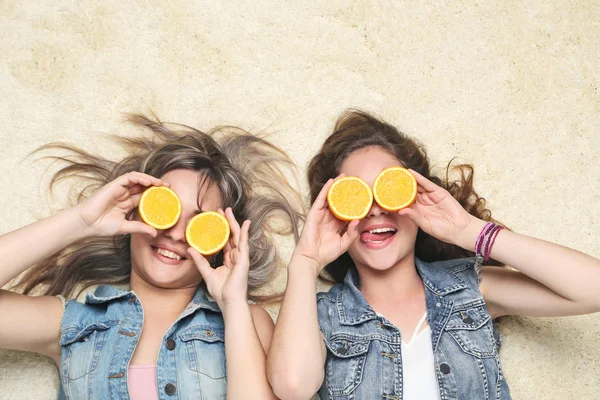 Dos mujeres jóvenes con fruta naranja en la alfombra — Foto de Stock