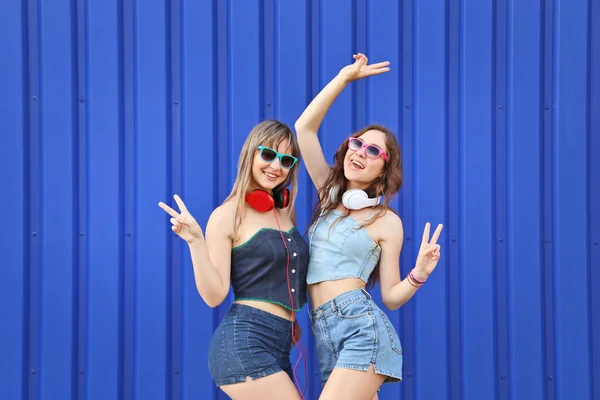 Dos mujeres jóvenes con gafas de sol y auriculares sobre fondo azul — Foto de Stock