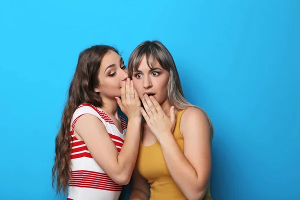 Două femei tinere șoptind un secret pe fundal albastru — Fotografie, imagine de stoc
