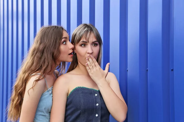 Две девушки шепчут тайну на голубом фоне — стоковое фото