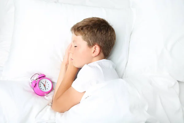 Jeune garçon avec réveil dormant dans un lit blanc — Photo