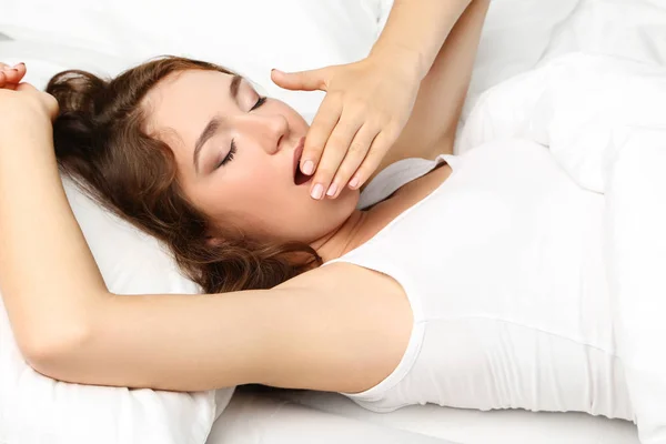 Mujer joven bostezando en la cama blanca — Foto de Stock