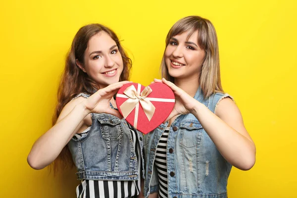 Dos mujeres jóvenes con caja de regalo sobre fondo amarillo — Foto de Stock