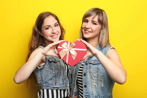 Duas jovens com caixa de presente no fundo amarelo — Fotografia de Stock